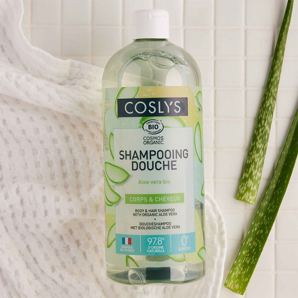 Flacon de shampooing avec feuilles d'aloe vera et serviette. Inscription: Coslys, Shampooing Douche, Aloe vera bio. Bio.