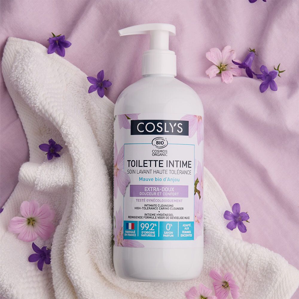 Witte fles met pomp. Label: Coslys, Toilette Intime, Extra-Doux. Op witte handdoek, versierd met bloemen.