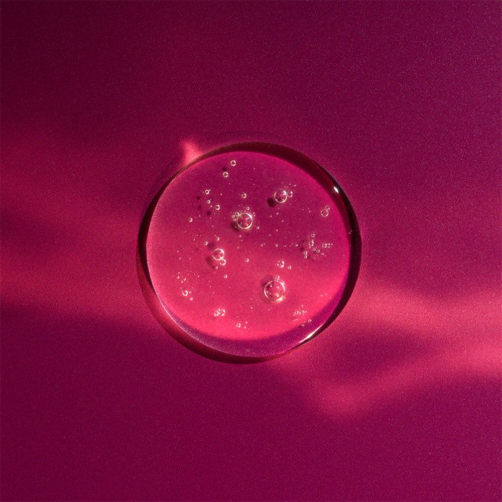 Ronde, roze vloeistofdruppel met belletjes. Roze achtergrond.