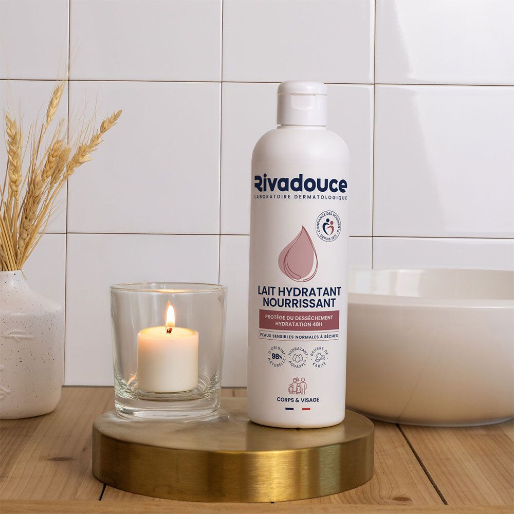 Witte fles met roze etiket. Opschrift: Rivadouce, Lait Hydratant Nourrissant. Op een sokkel met kaars en decoratie.