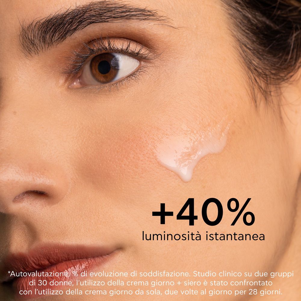 Close-up van een gezicht met aangebrachte vloeistof. Tekst: +40% luminosità istantanea.