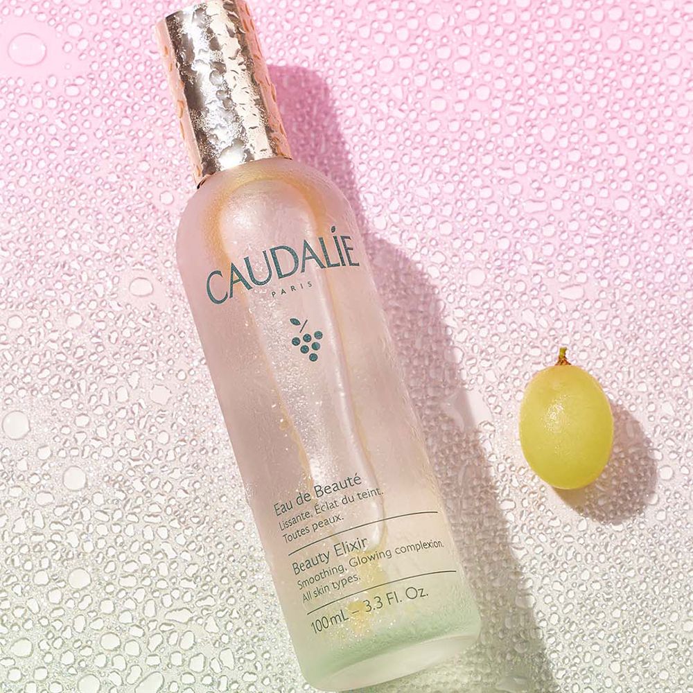 Gros plan du bouchon du flacon Caudalie Eau de Beauté. Bouchon argenté avec gouttes. Texte: Caudalie.