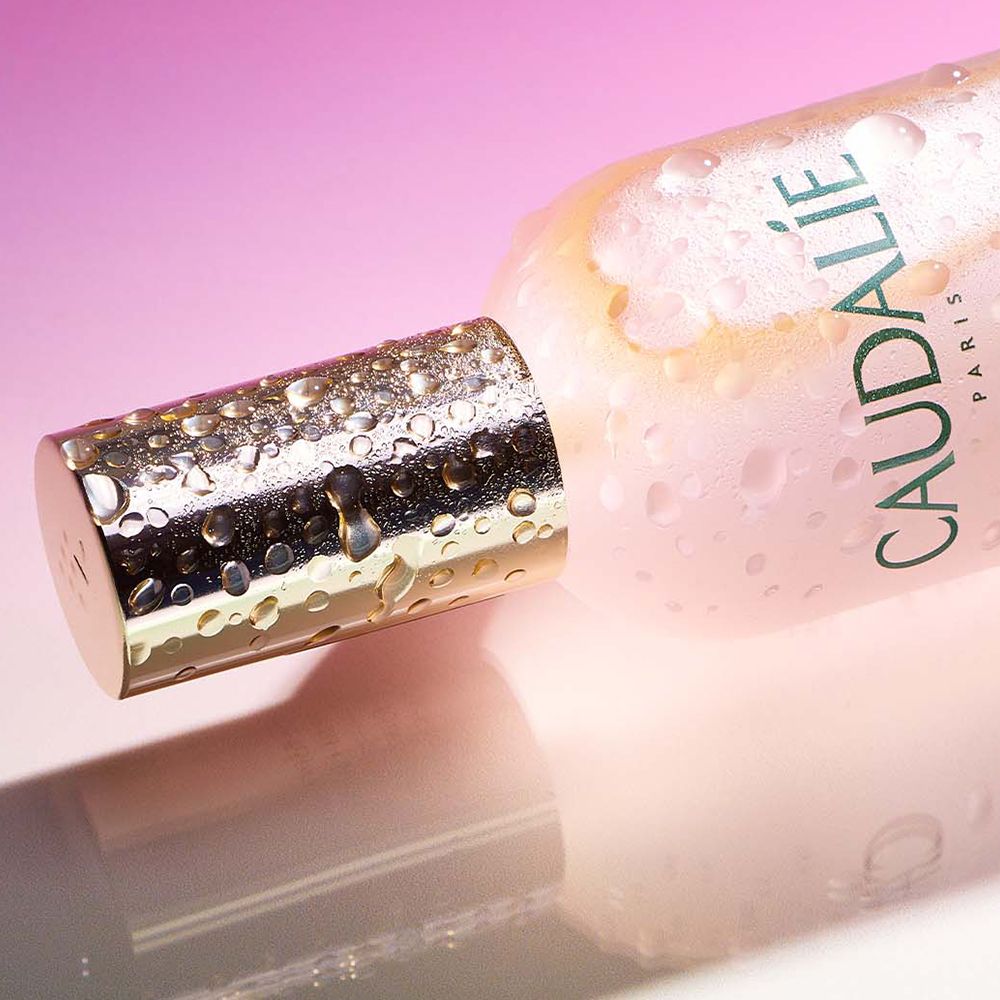 Gros plan du bouchon du flacon Caudalie Eau de Beauté. Bouchon argenté avec gouttes. Texte: Caudalie.