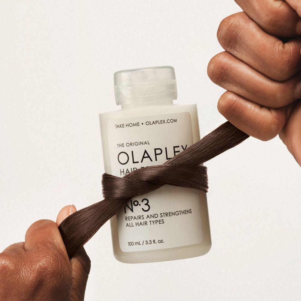 Olaplex No. 3 fles, omwikkeld met bruin haar. Handen houden het haar stevig vast.