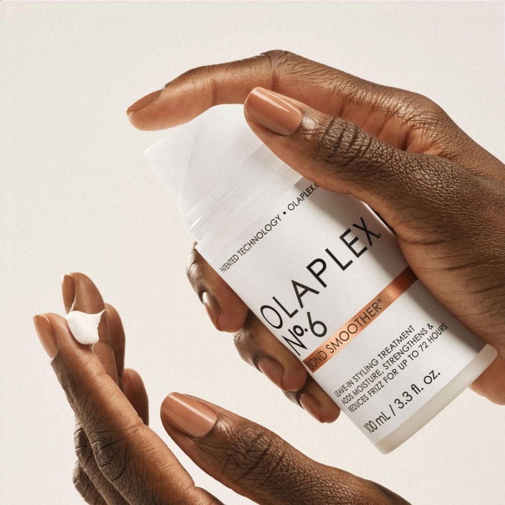 Handen houden een witte fles vast. Opschrift: OLAPLEX No.6 Bond Smoother. Product op vinger.