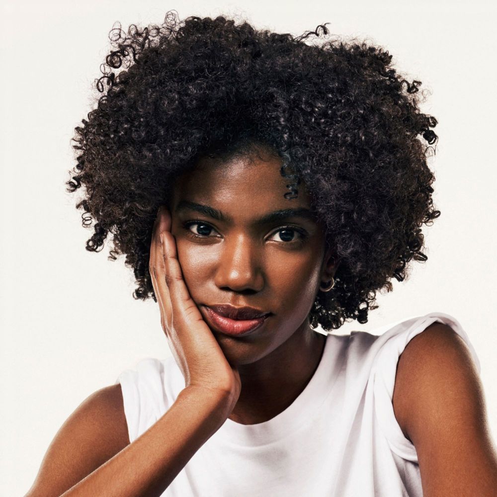 Portrait d'une femme aux cheveux bouclés. Elle touche sa joue avec sa main.