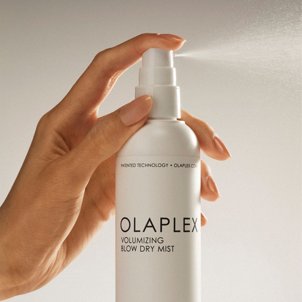 Main vaporisant Olaplex Volumizing Blow Dry Mist. Flacon blanc, brume visible.