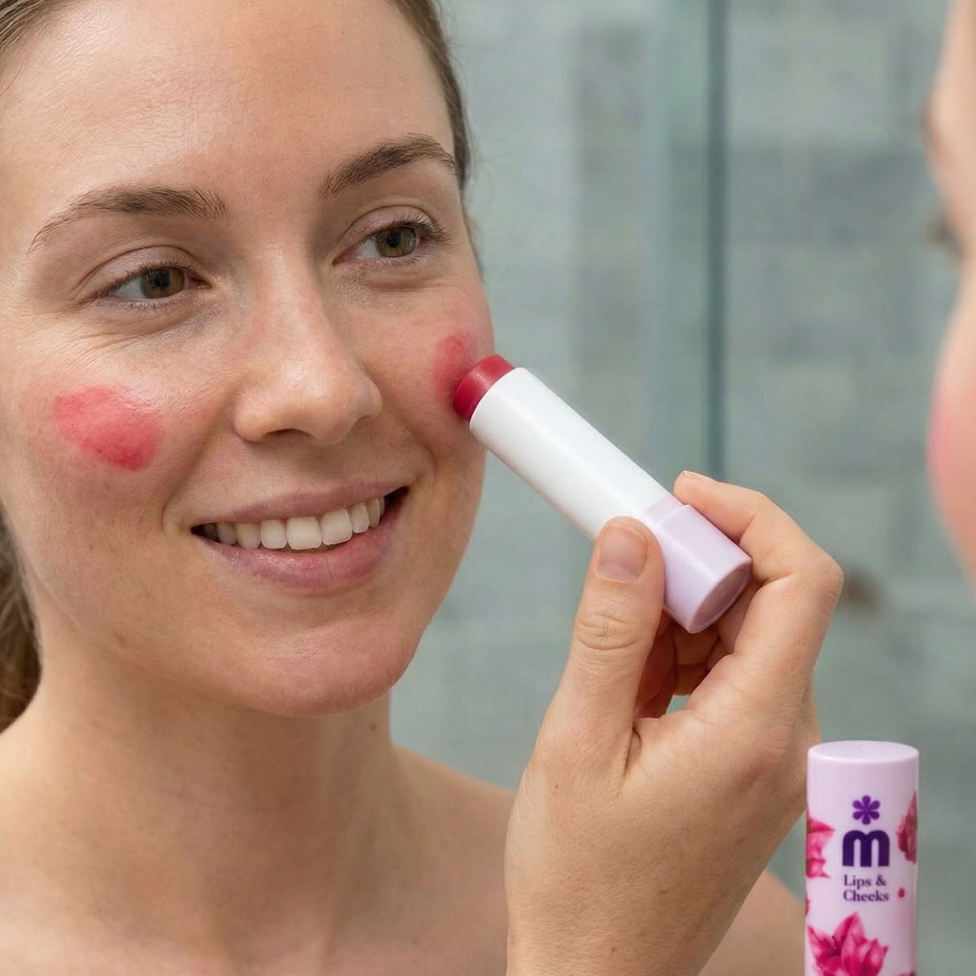 Femme appliquant un baume lèvres et joues. Nom du produit: Melem Lips & Cheeks. Bâton blanc avec embout rose. Miroir en arrière-plan.