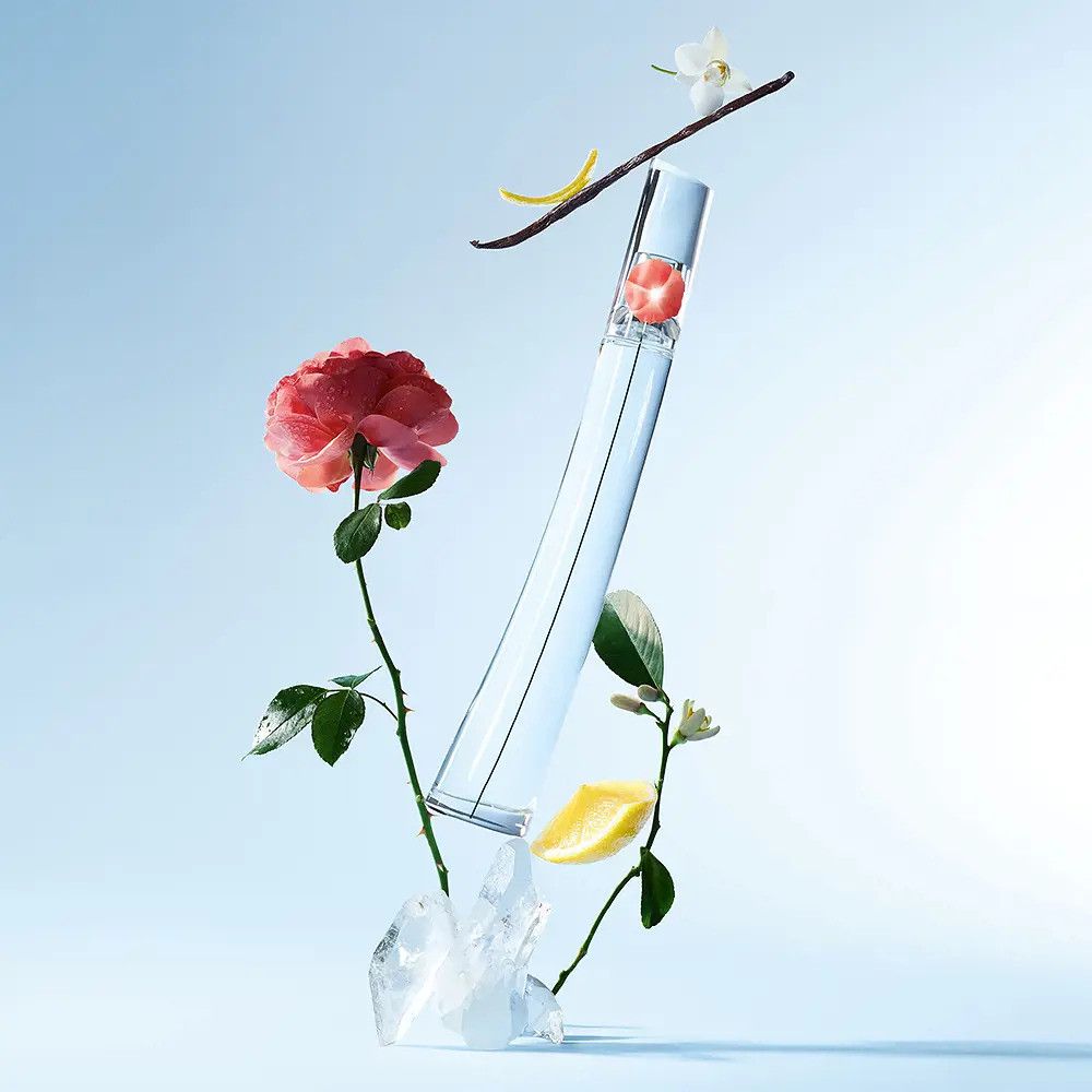 Flacon transparent avec fleur rouge, entouré de fleurs, citron, vanille et glace. Sur fond bleu.