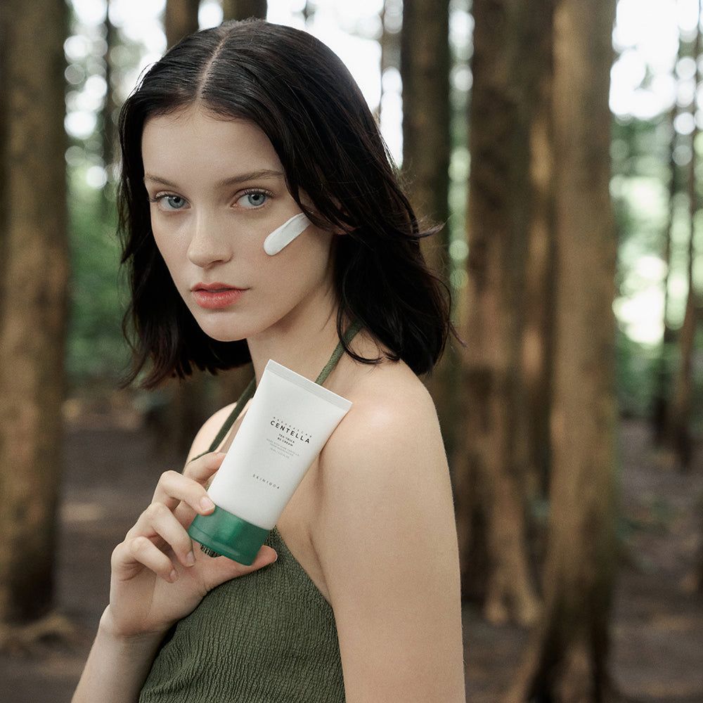 Vrouw houdt tube crème vast. Aangebracht op wang. Achtergrond: bomen. Opschrift: CENTELLA, TEA-TRICA B5 CREAM.