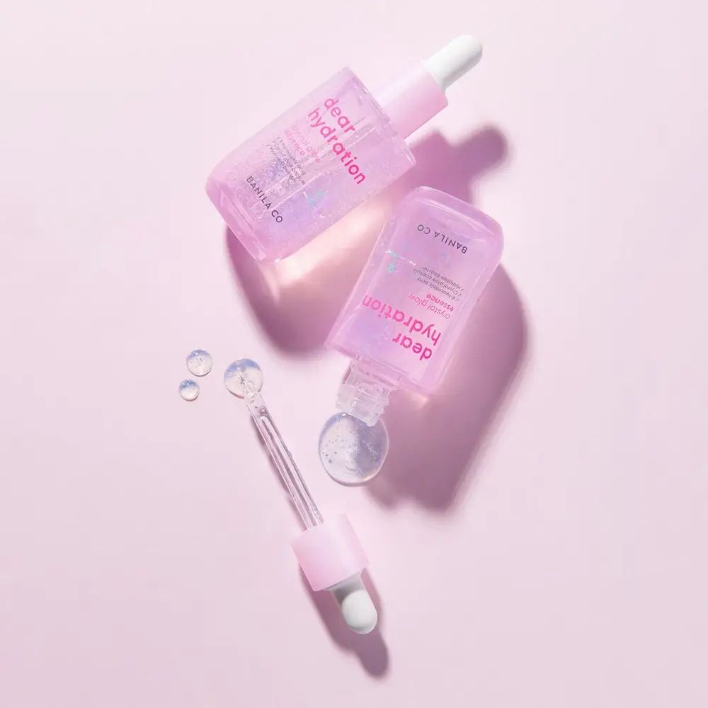 Twee flesjes BANILA CO Dear Hydration Crystal Glow Essence. Roze flesjes met pipetten en transparante druppels.