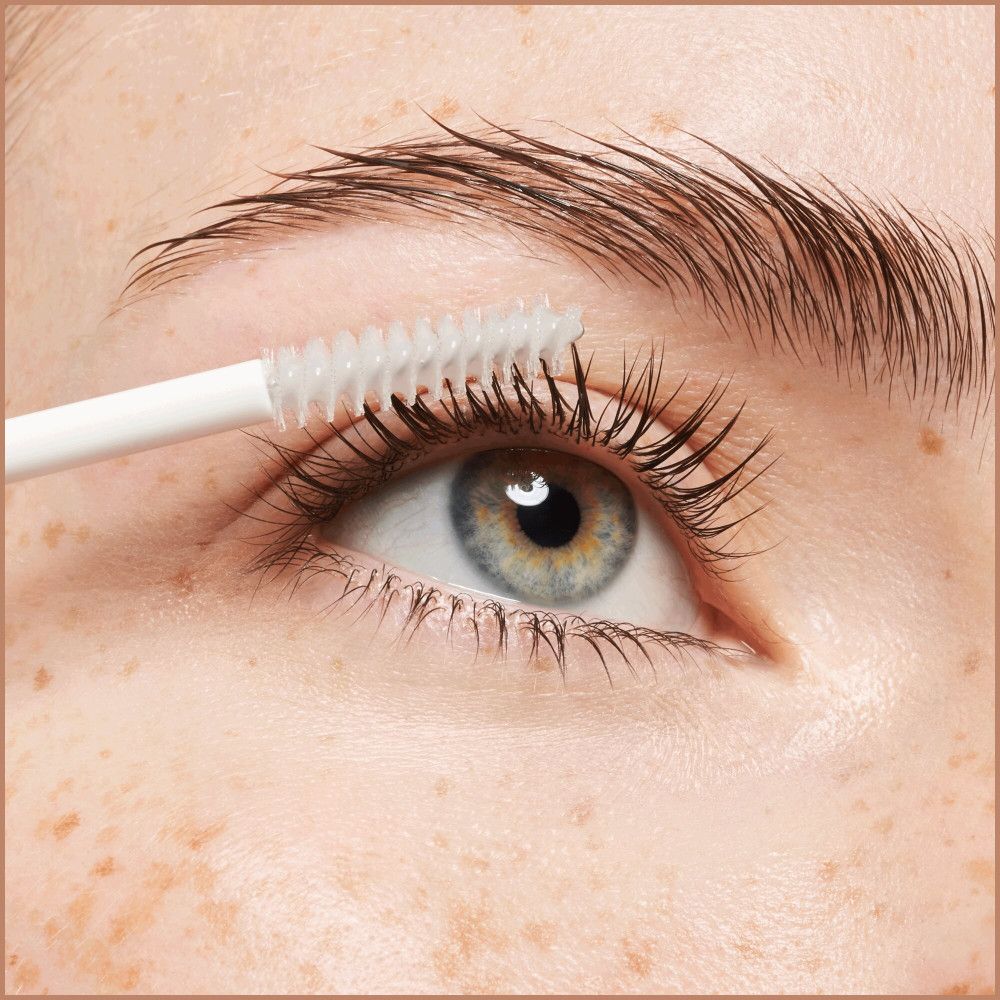 Œil avec sourcil. Brosse appliquant le sérum sur les cils. Peau avec des taches de rousseur.