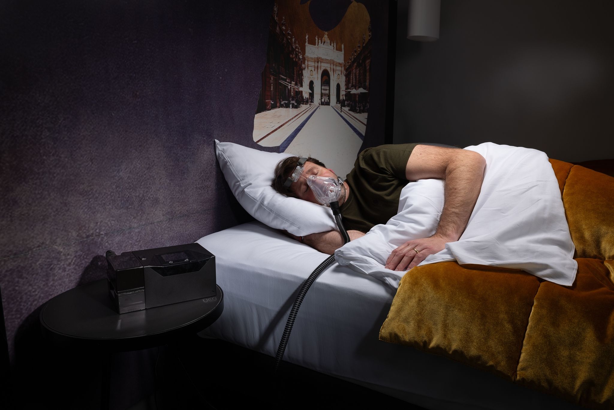 Man slaapt met masker op bed. APAP-apparaat naast het bed.