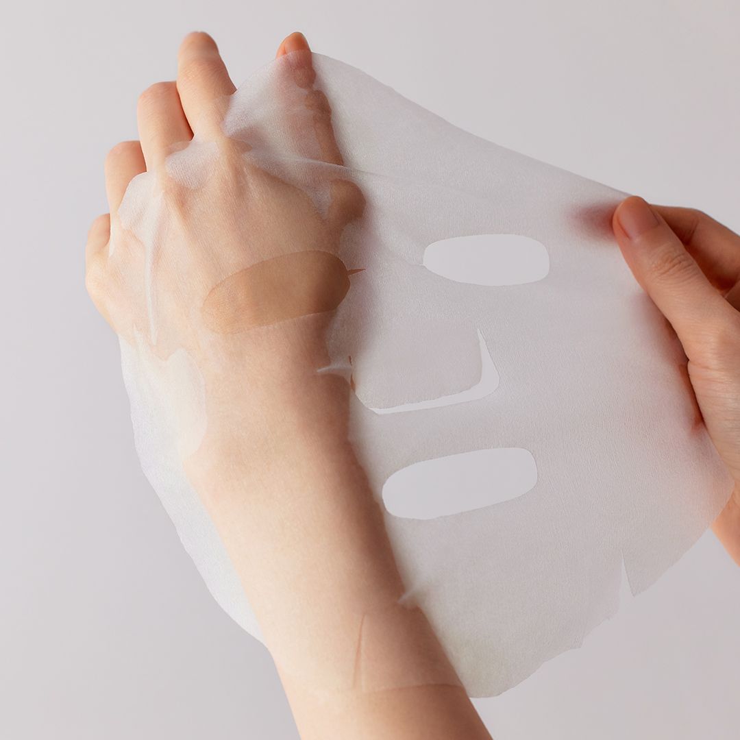 Handen houden een transparant gezichtsmasker vast. Het masker heeft openingen voor ogen, neus en mond.