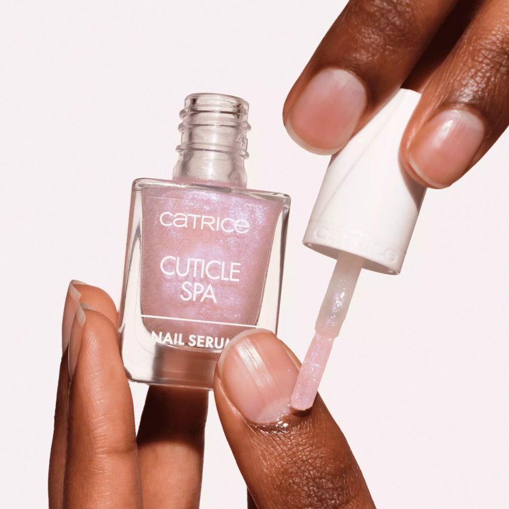 Mains tenant un flacon de liquide rose et un pinceau. Inscription : Catrice, Cuticle Spa, Nail Serum. Pinceau touchant un ongle.
