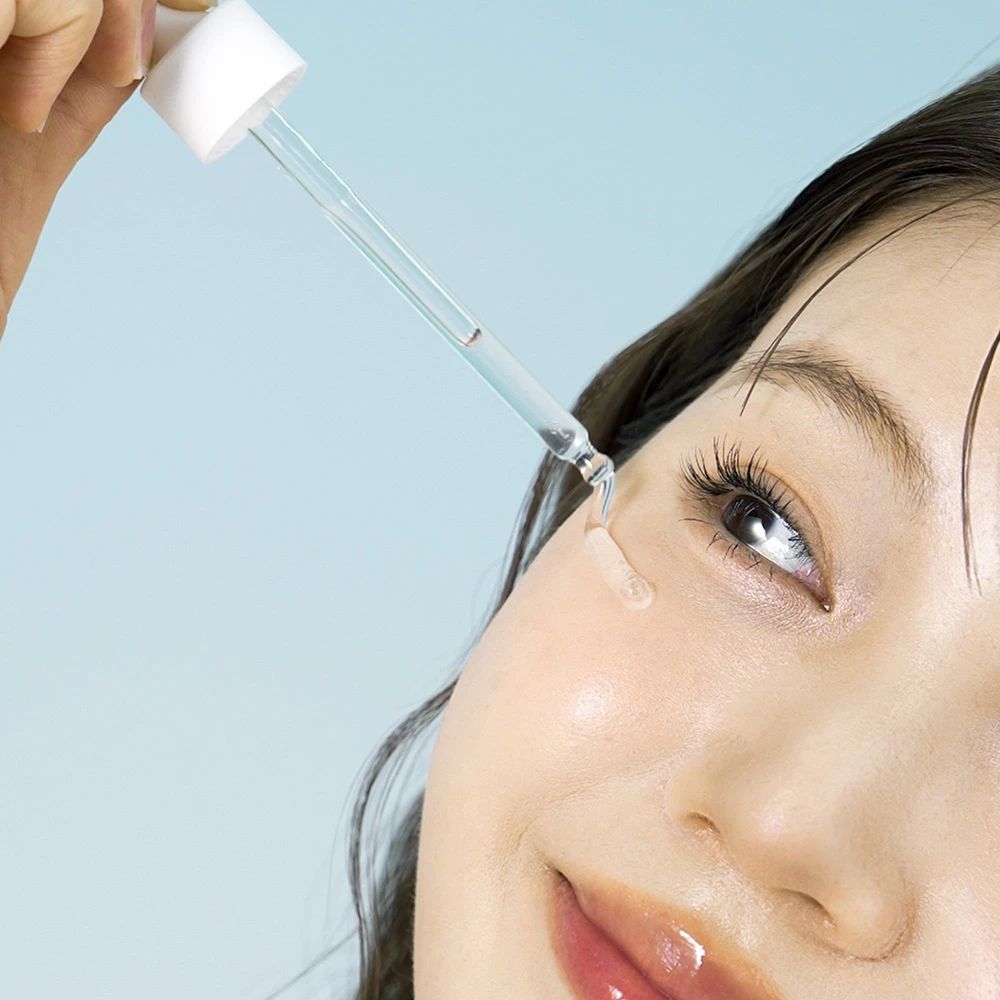 Vrouw met serum applicator. Serum wordt op de huid aangebracht. Blauwe achtergrond.