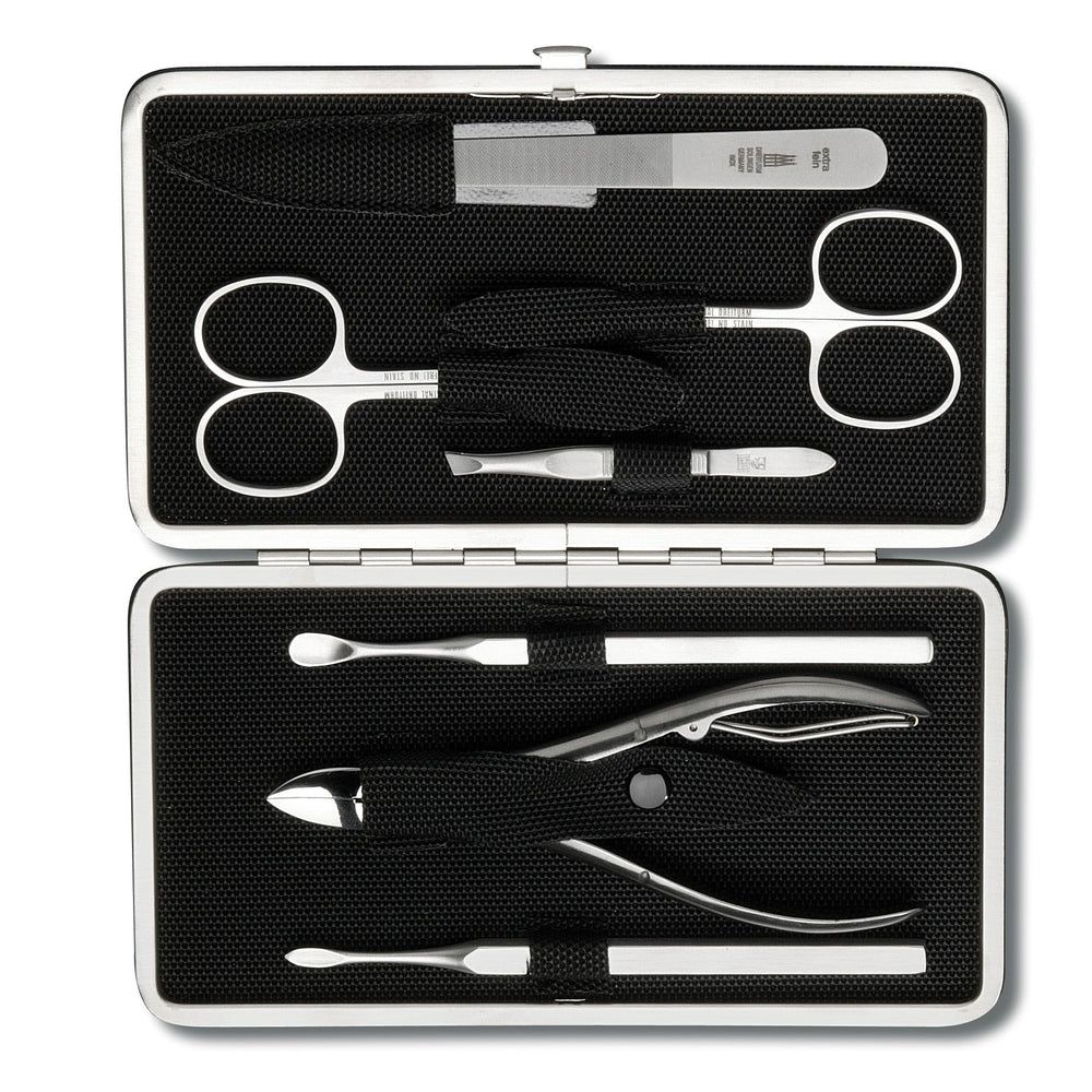 Étui de manucure ouvert avec outils argentés sur tissu noir. Comprend ciseaux, lime, coupe-ongles et autres instruments.