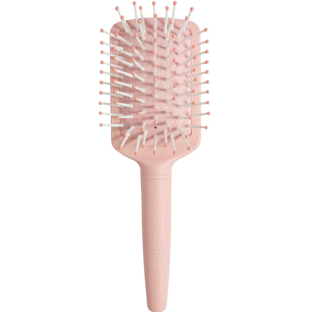 Une brosse à cheveux rectangulaire rose pâle avec des picots blanc-rose et un manche court.