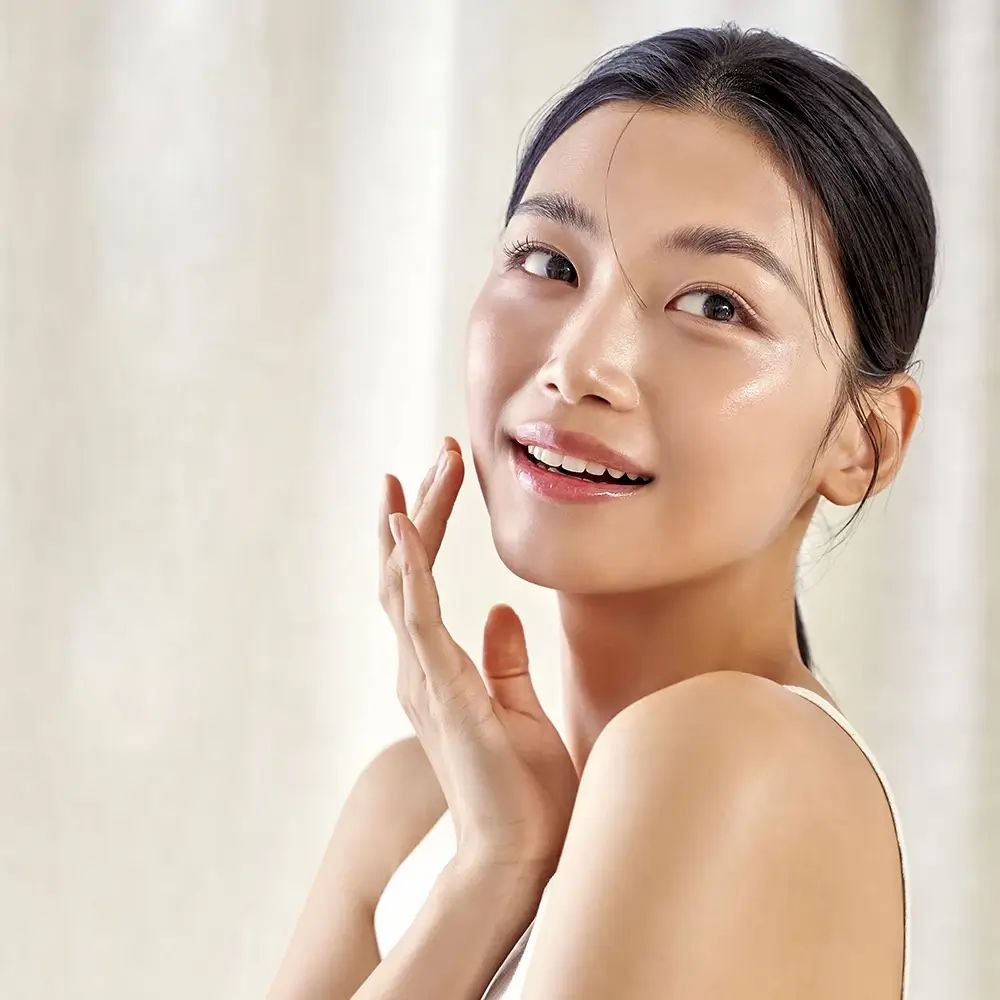 Vrouw raakt haar gezicht aan. Lichte huid, witte top. Lichte achtergrond.