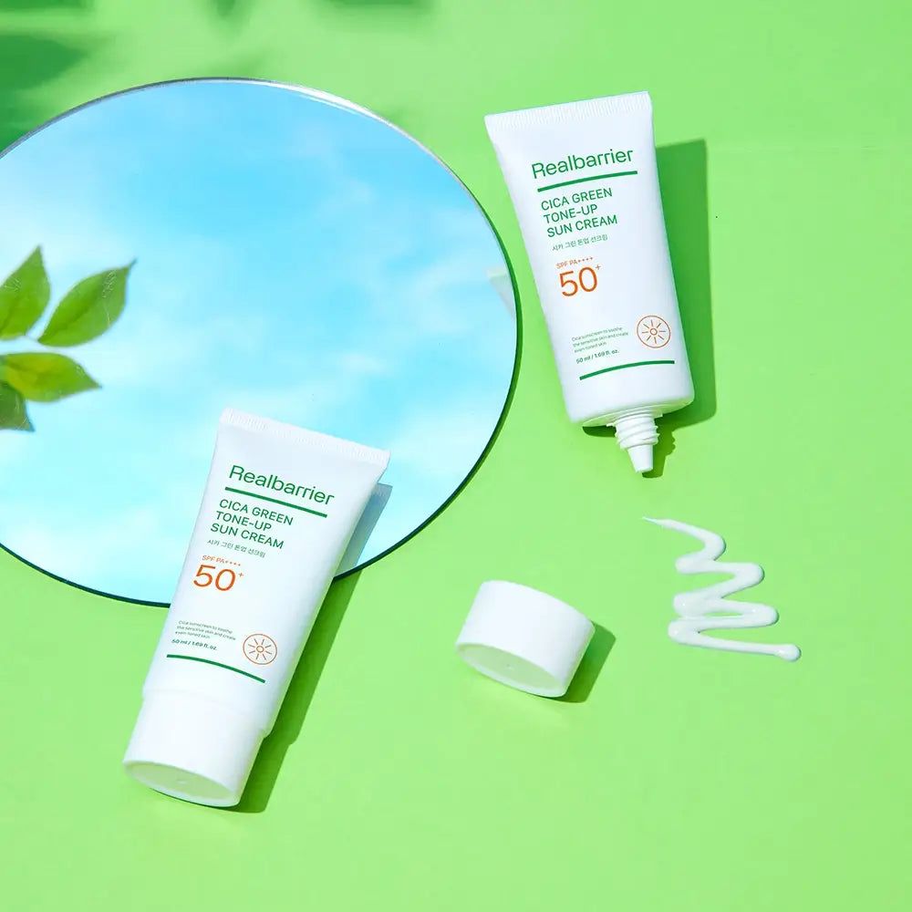 Deux tubes de crème solaire Real Barrier, un avec bouchon ouvert, une goutte de crème à côté. Miroir en arrière-plan.