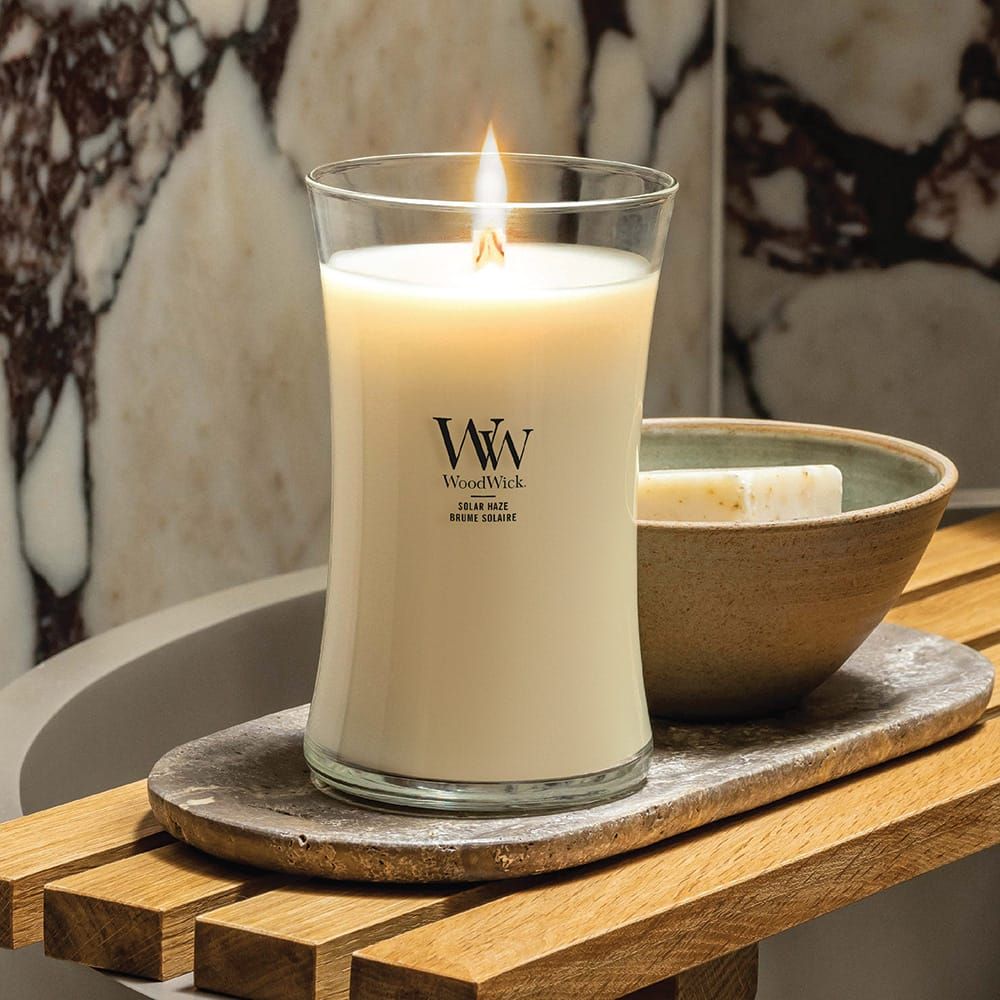 Bougie allumée dans un verre. Marque WoodWick visible. Accompagnée d'un savon et d'un bol sur un plateau en bois.