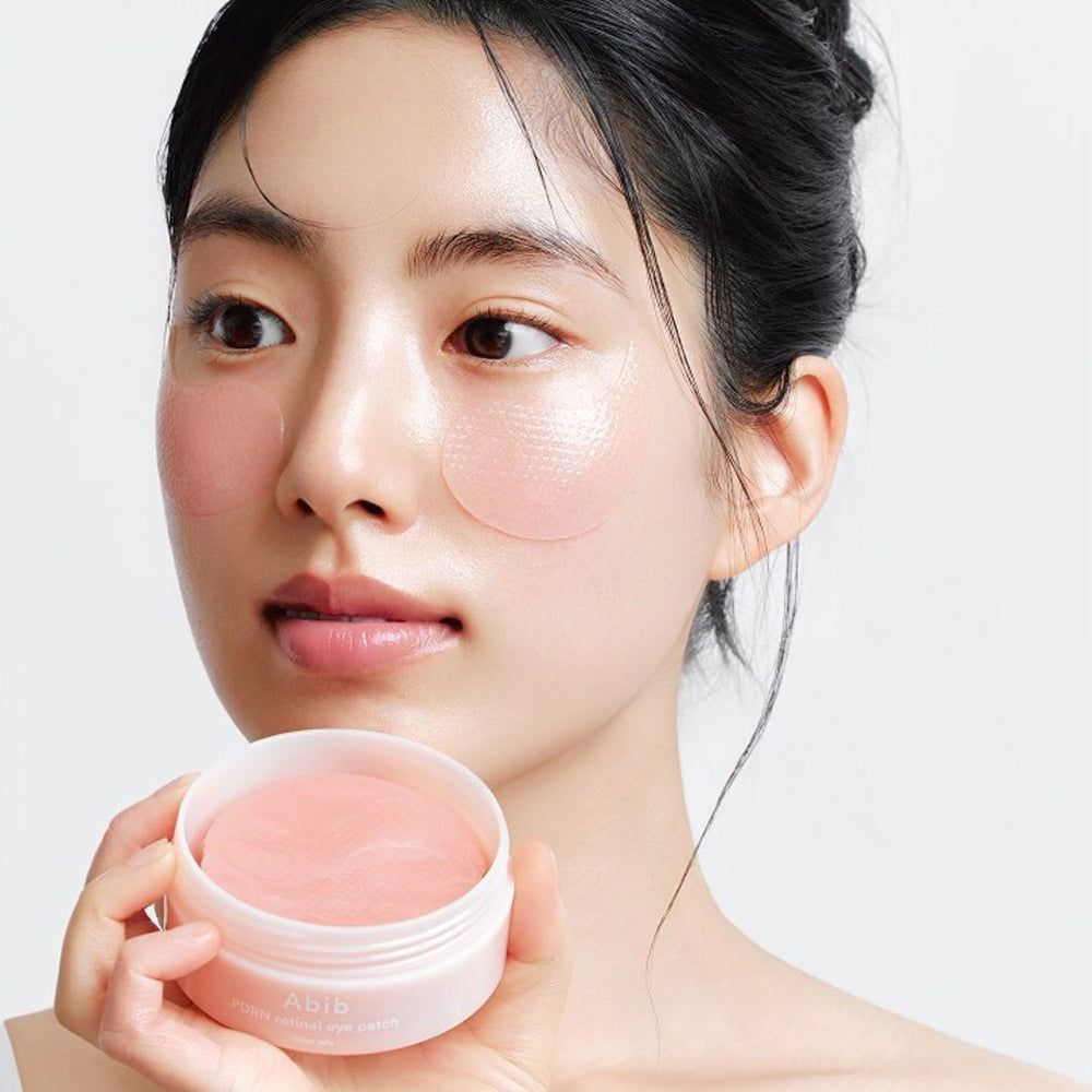 Femme tenant un pot ouvert de patchs pour les yeux. Des patchs pour les yeux sont appliqués sur la peau. Pot avec inscription Abib.