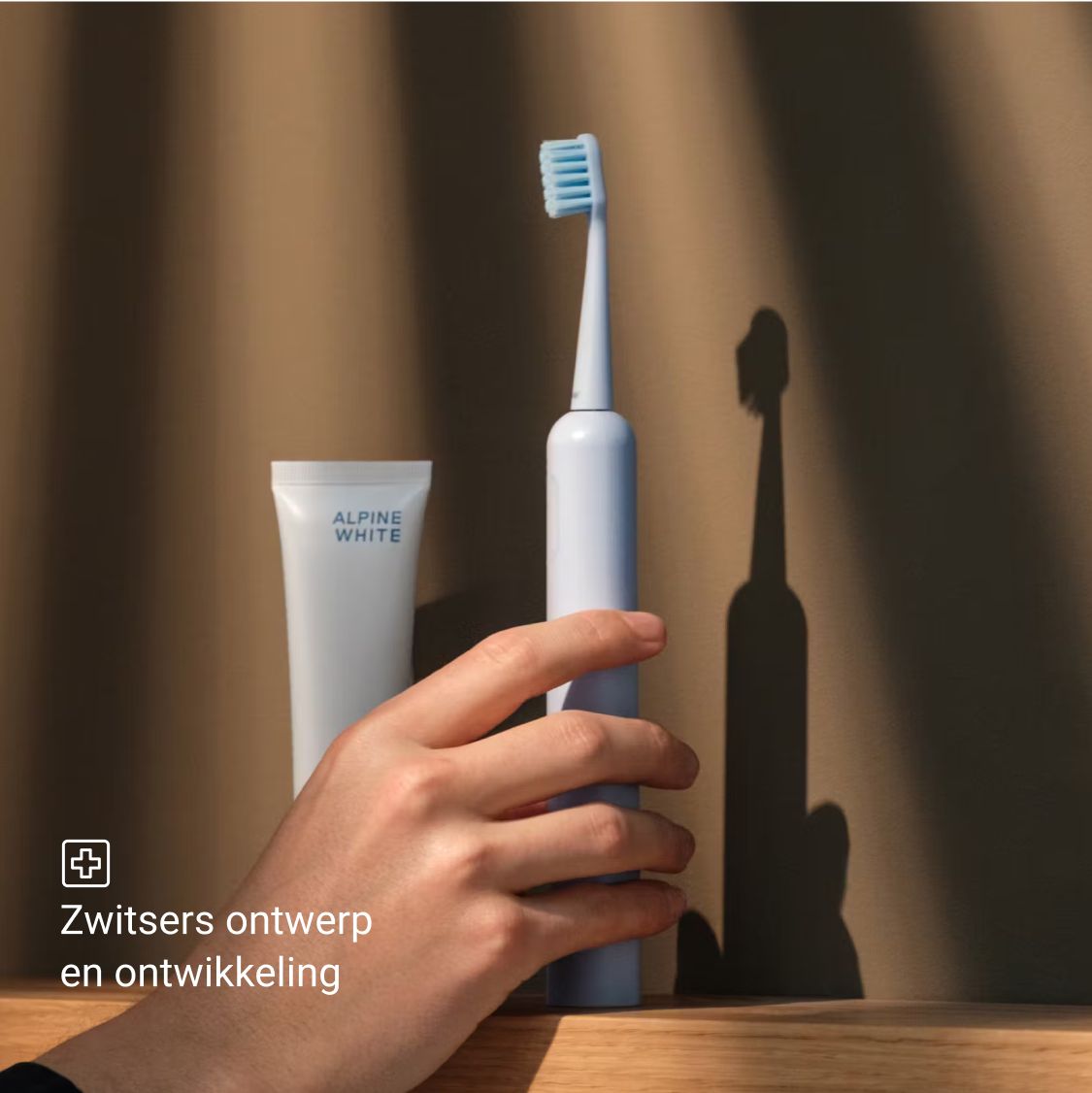 Een blauwe elektrische tandenborstel, tandpasta en een hand. Zwitsers ontwerp en ontwikkeling.