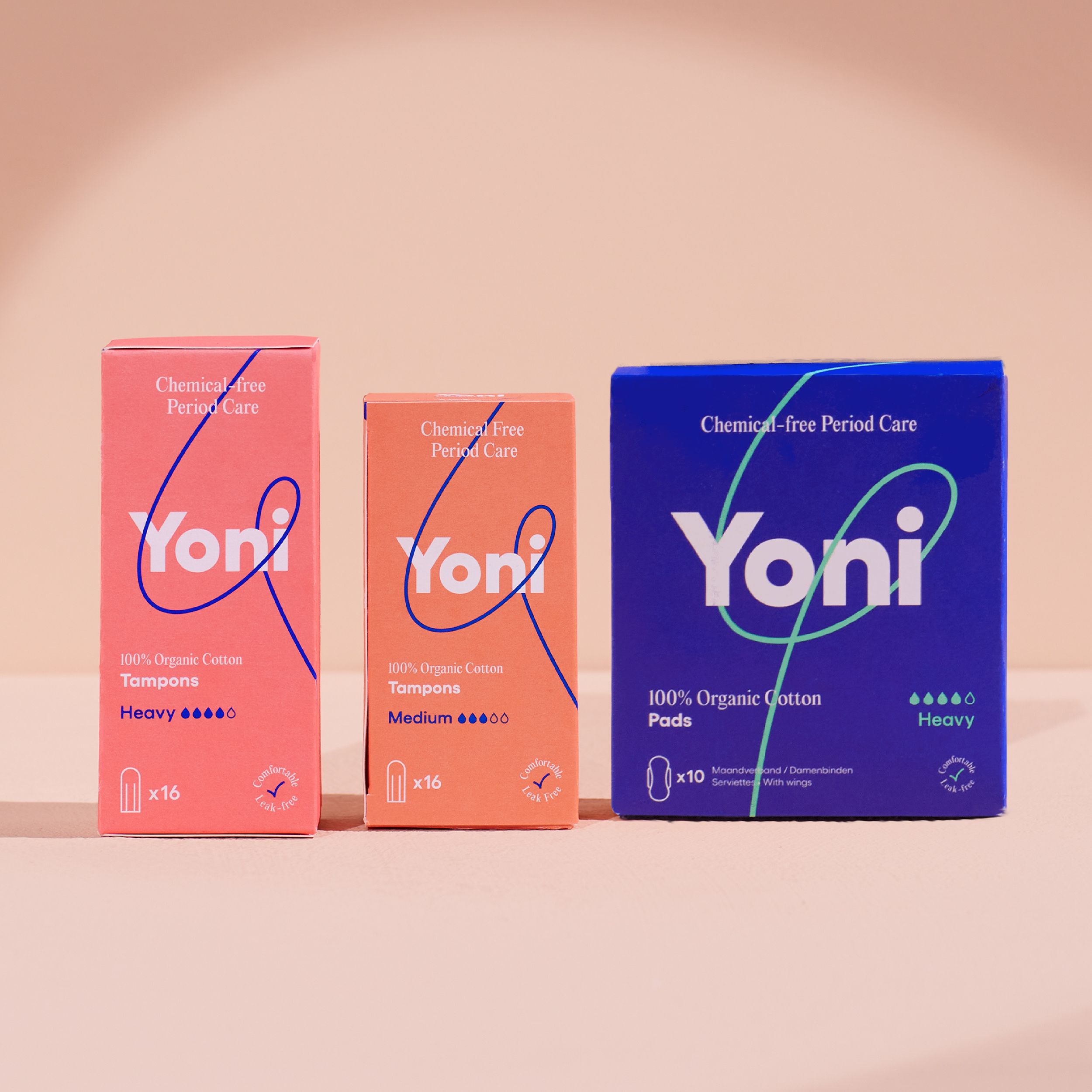 Trois boîtes de produits d'hygiène féminine. Logo Yoni. Rose, orange et bleu. Inscriptions : Tampons, Pads, Heavy, Medium.
