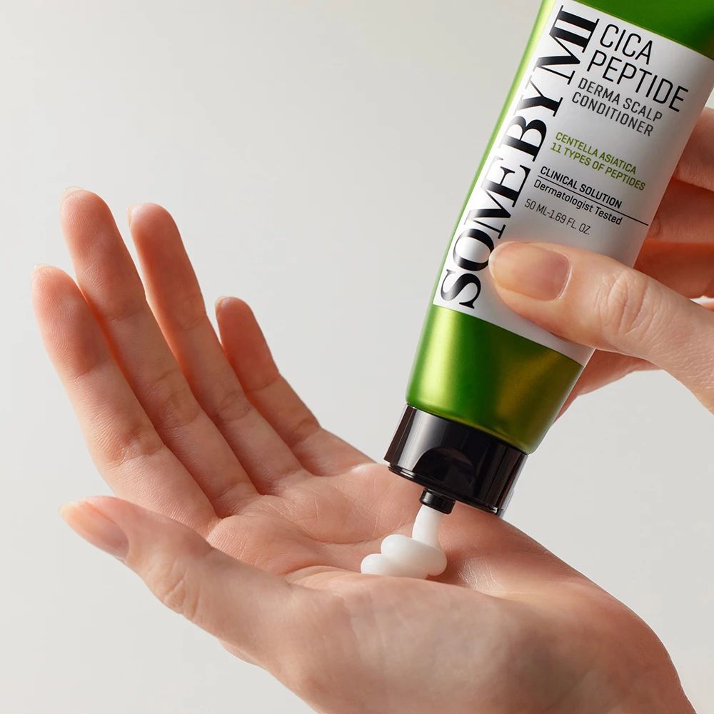 Tube vert SOME BY MI Cica Peptide. Crème blanche sortant du tube. Main en dessous. Fond clair.