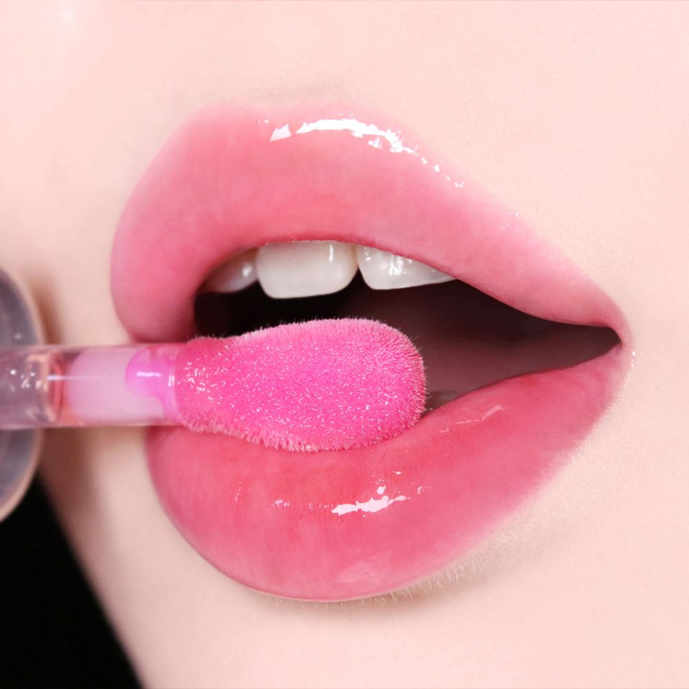 Gros plan sur des lèvres recouvertes d'un applicateur rose de gloss à lèvres brillant.
