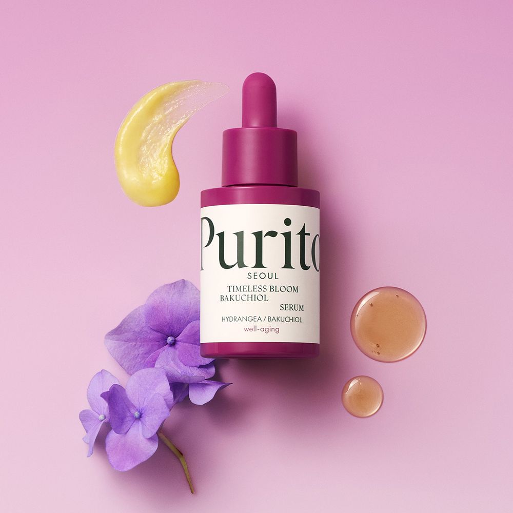 PURITO Timeless Bloom Bakuchiol Serum flesje. Paarse bloemen, gele serumvlek. Roze achtergrond.