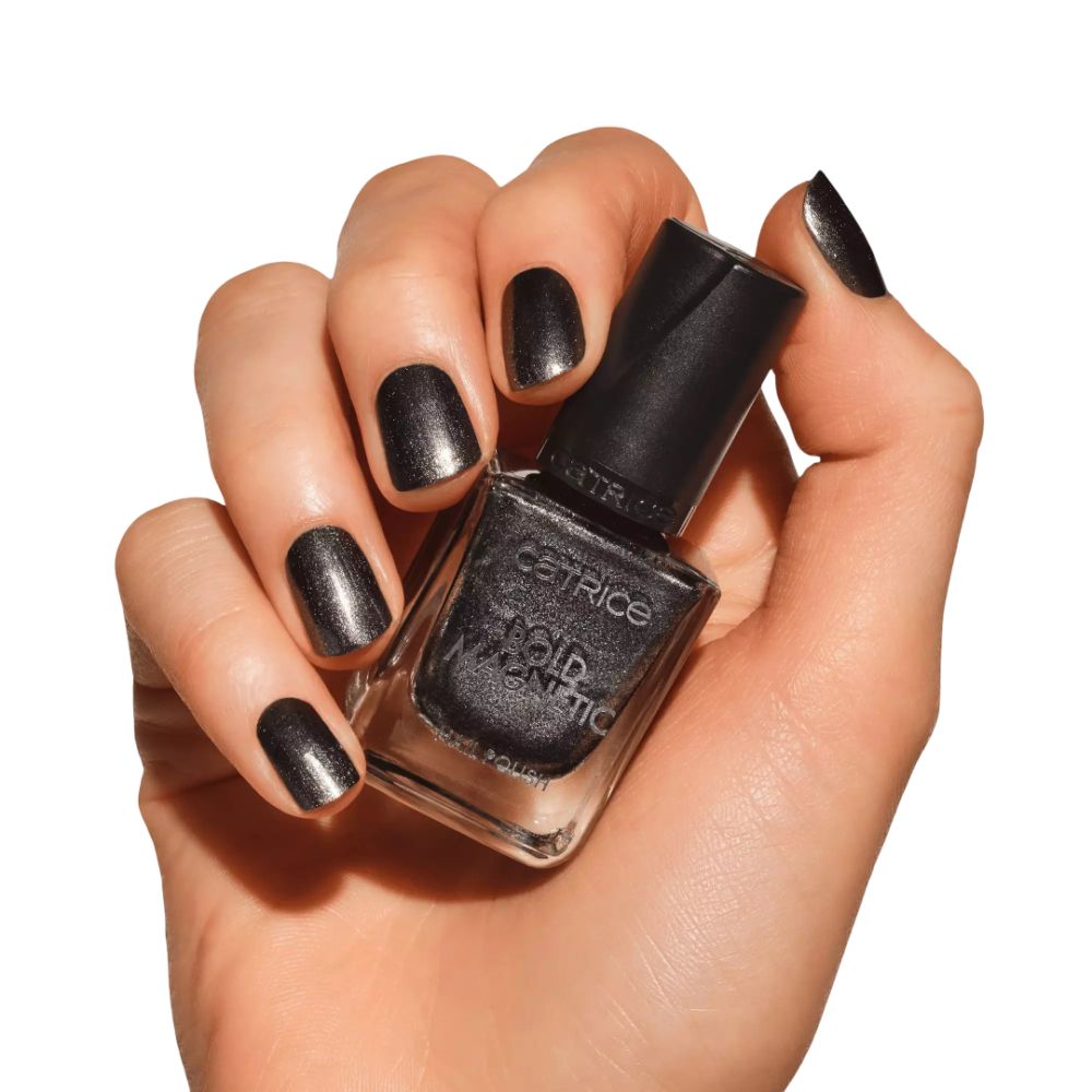 Main avec ongles vernis et flacon de vernis à ongles. Inscription : Catrice, Bold Magnetic, Nail Polish. Flacon tenu.