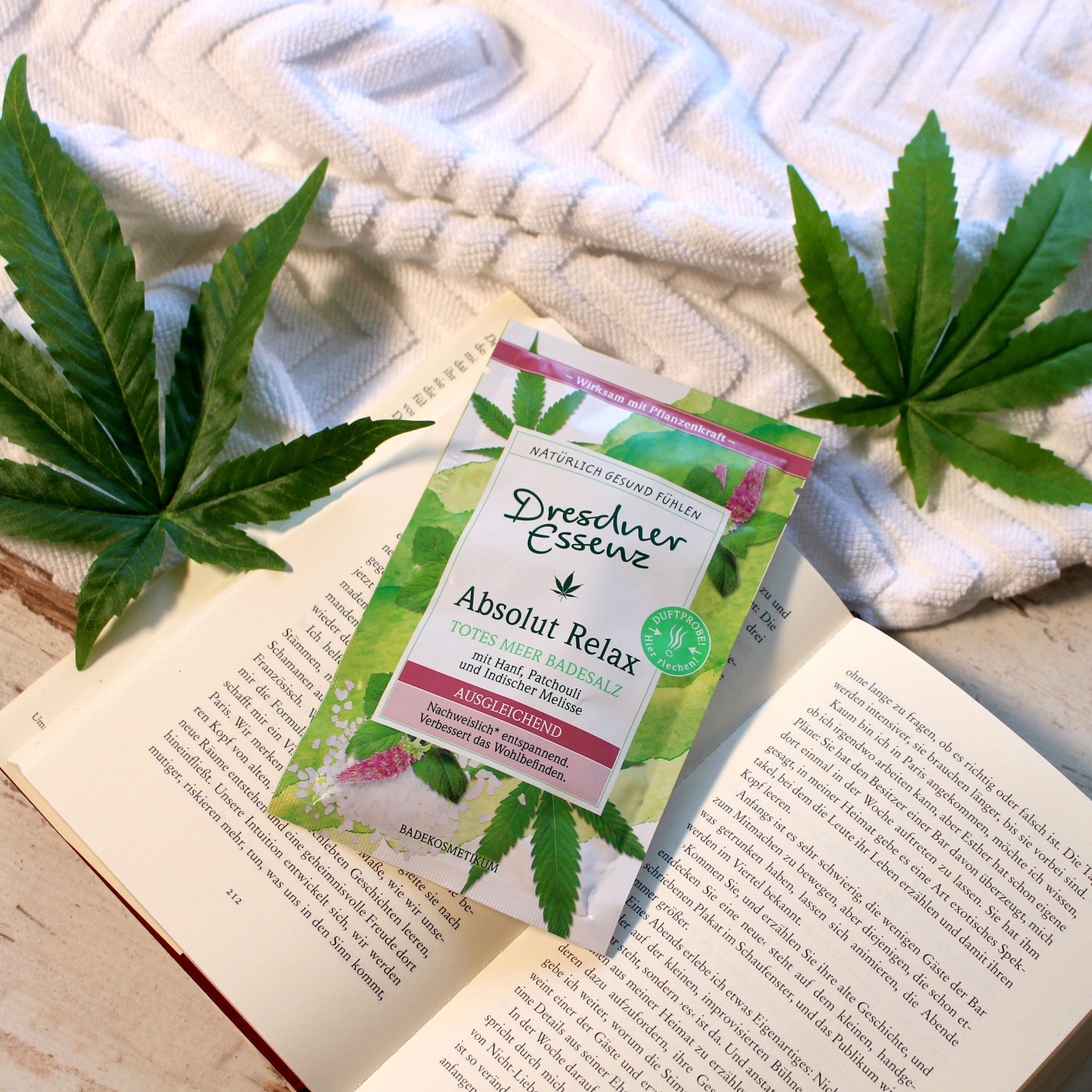 Productverpakking met badzout op een boek en naast bladeren. Productnaam en ingrediënten zijn zichtbaar.