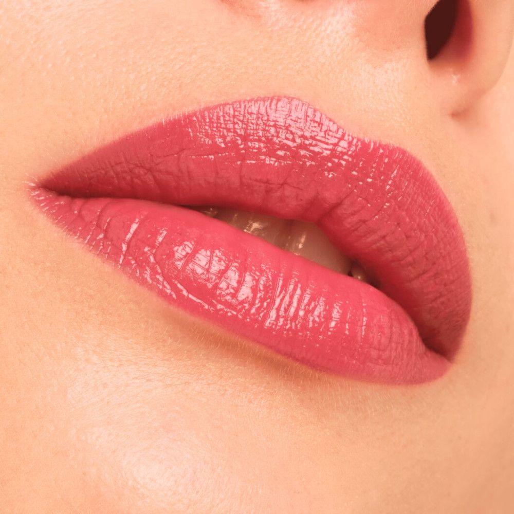 Gros plan sur des lèvres avec un rouge à lèvres brillant rose. Les lèvres sont légèrement entrouvertes.