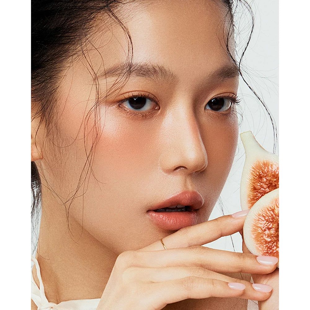 Portrait d'une femme avec du fard à joues. Des moitiés de figues sont visibles à côté.