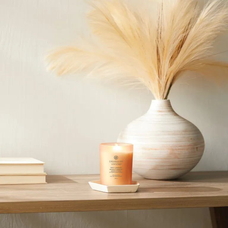 Bougie parfumée dans un récipient en verre. Sur un dessous de plat blanc. Près d'un vase avec des herbes de la pampa.
