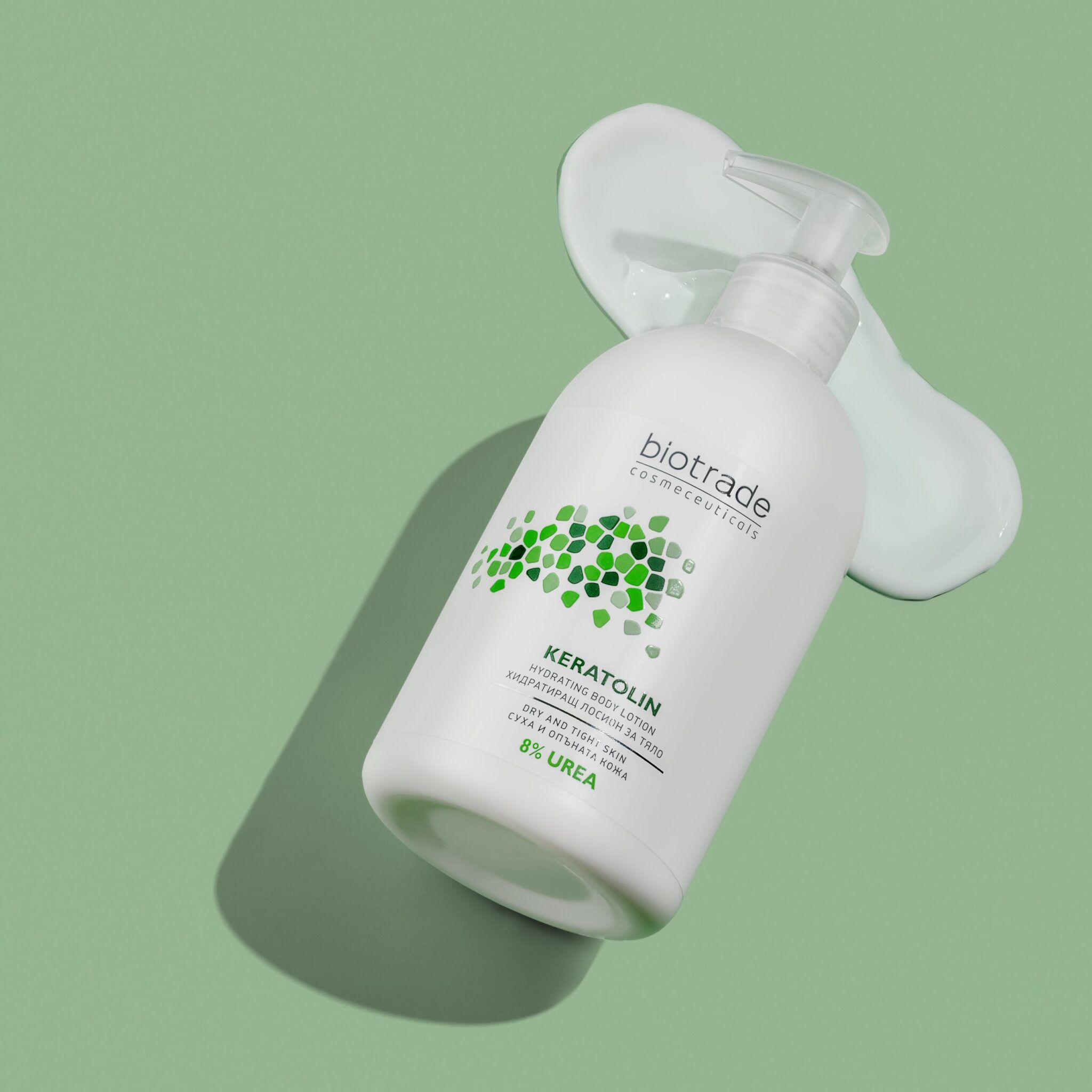 Flacon blanc avec pompe. Biotrade Keratolin Body, 8% Urée. Liquide verdâtre à côté. Sur fond vert.