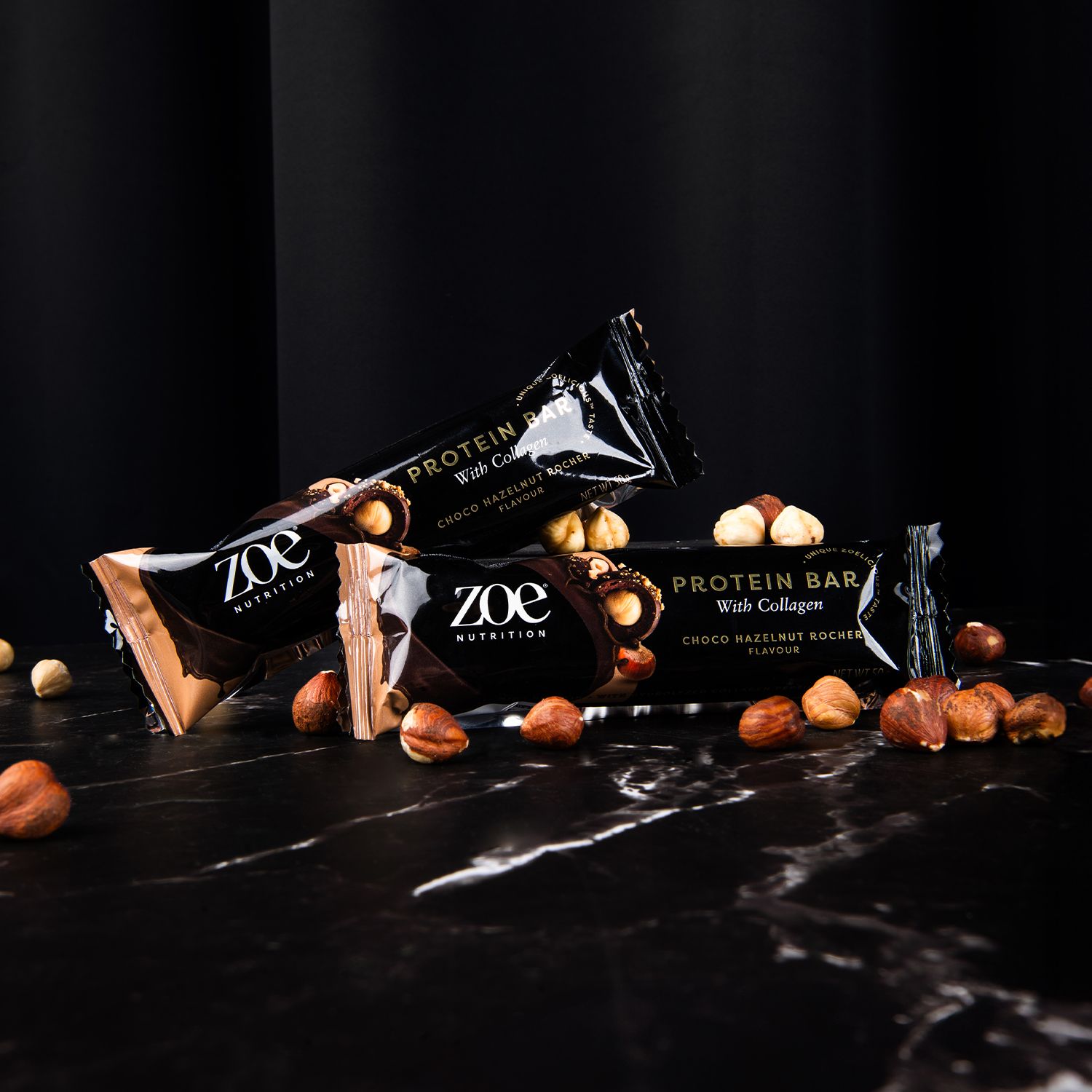 Drie eiwitrepen met collageen en hazelnoten op zwart marmer. Logo en productnaam zichtbaar. Donkere achtergrond.
