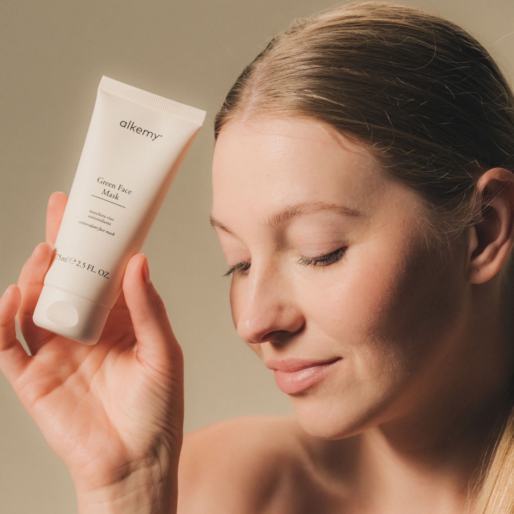 Une femme tient un tube blanc de masque facial vert Alkemy.
