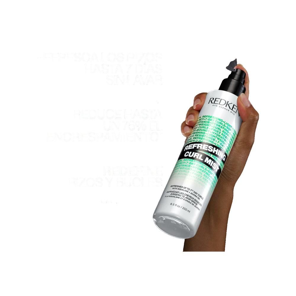 Hand die Redken Refreshing Curl Mist vasthoudt. Witte fles met zwarte sproeikop. Tekst: Refreshing Curl Mist, Redken, 5th Avenue NYC.