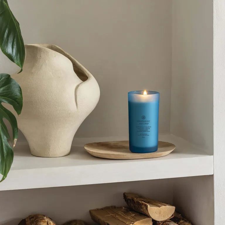 Bougie bleue allumée sur plateau bois. Chesapeake Bay, mind & body, confidence + freedom. Sur étagère.