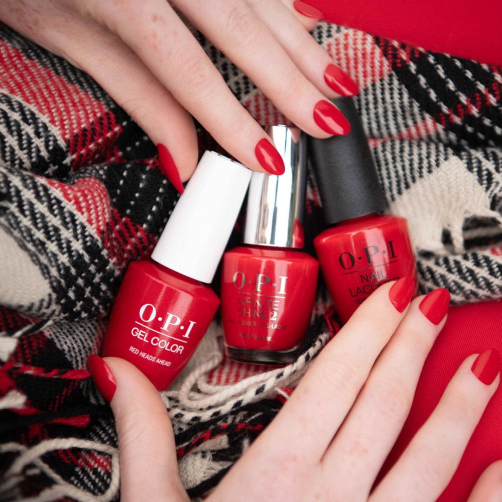 Trois flacons de vernis à ongles rouges OPI. Mains avec vernis rouge. Sur écharpe à carreaux.