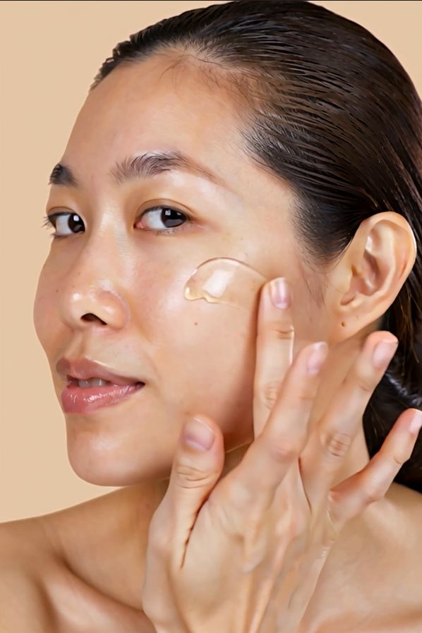 Vrouw brengt serum aan op haar gezicht. Lichte huid, bruin haar, beige achtergrond.