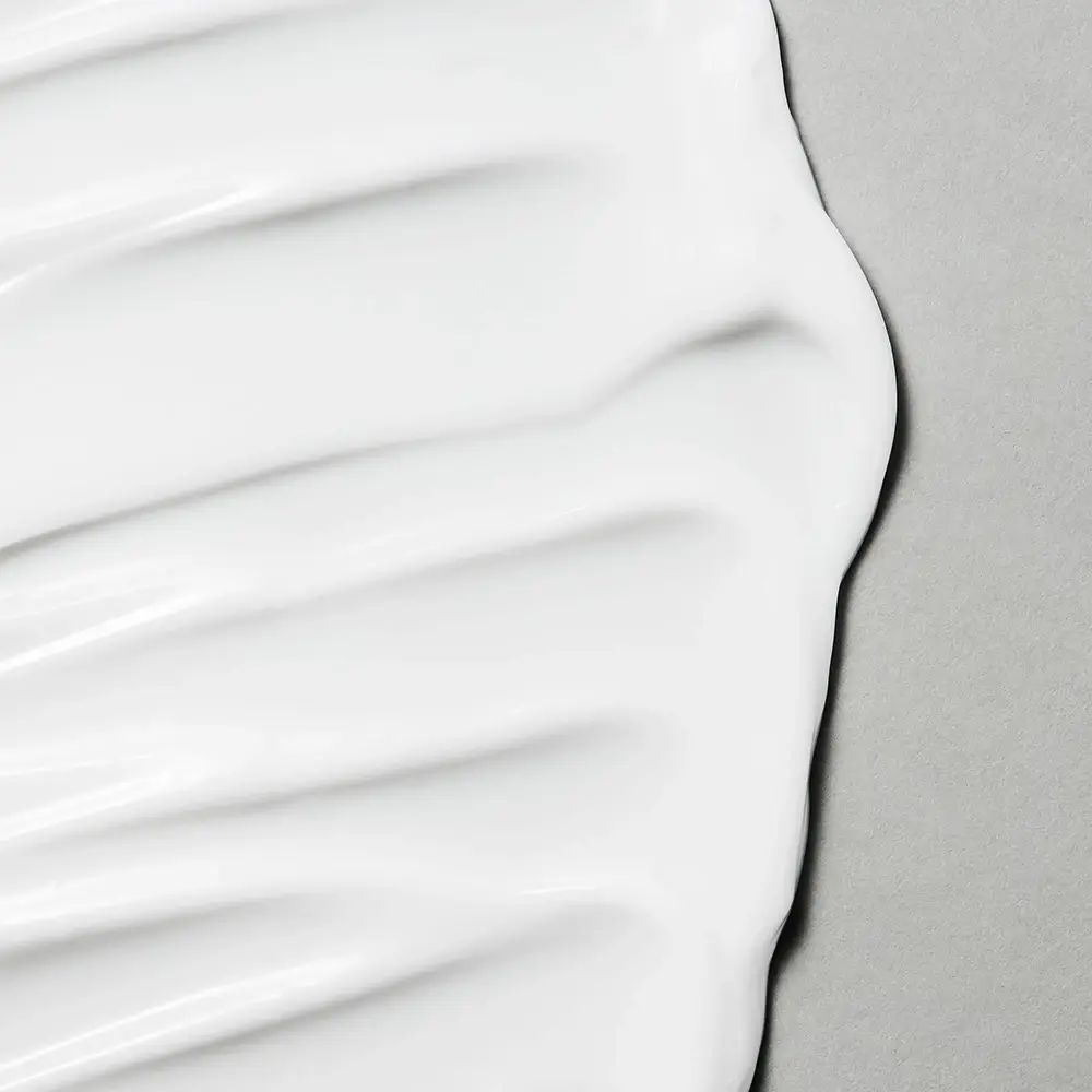 Close-up van witte crème. De textuur is glad en golvend. Grijze achtergrond.