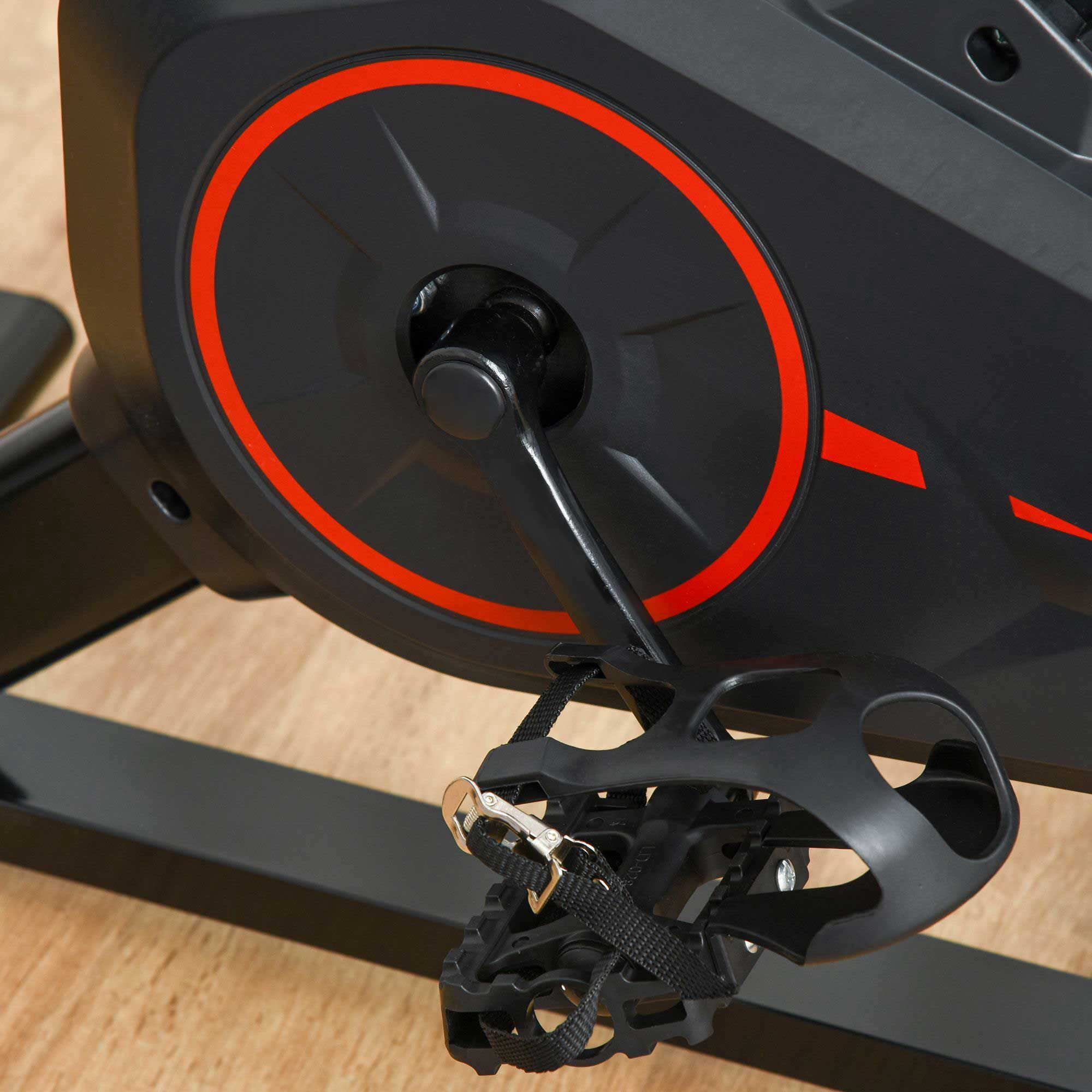 Close-up van de pedalen van een fitnessfiets. Zwarte kleur met riemen. Op houten vloer.