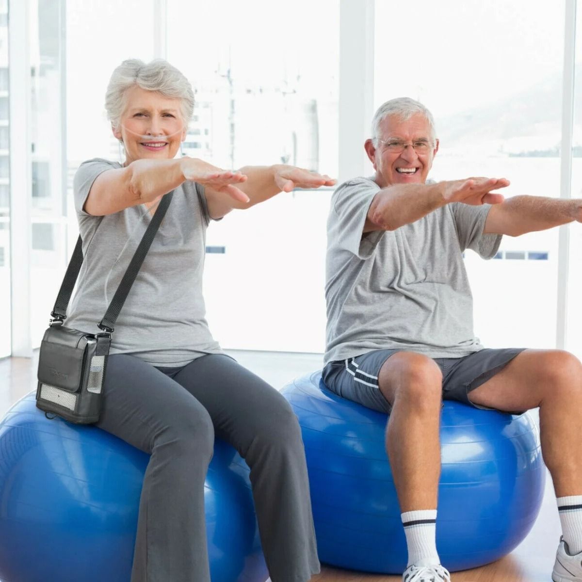 Ouder echtpaar met zuurstofconcentrator tijdens gymnastiek op fitnessballen.