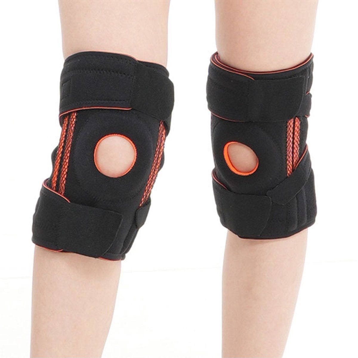 Deux genouillères noires avec détails orange. Fermetures velcro et ouverture pour la rotule. Portées sur les jambes.