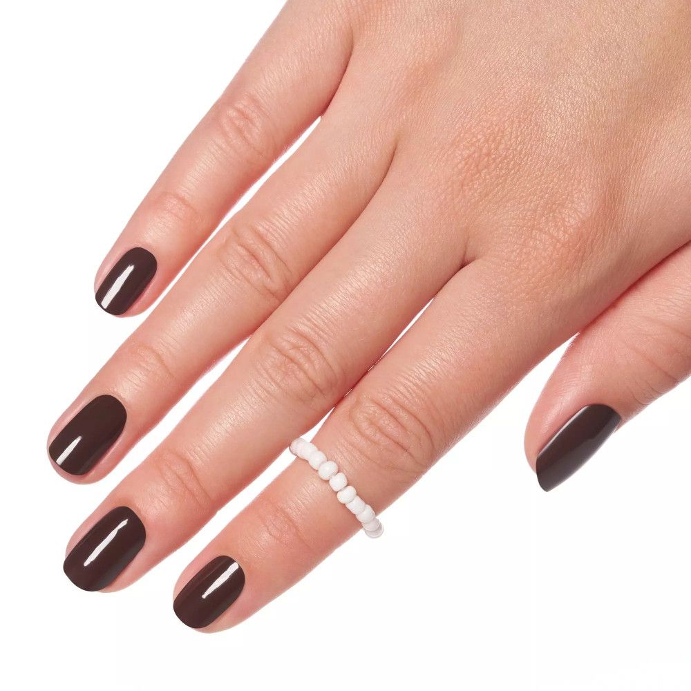 Main avec ongles vernis. Couleur marron. Bague de perles blanches sur l'annulaire.