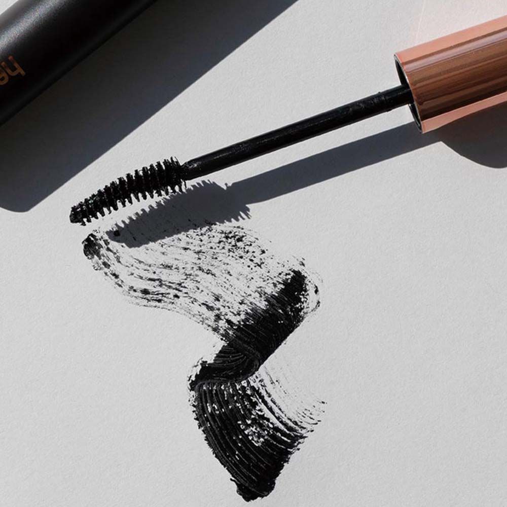 Applicateur de mascara avec brosse et trace de mascara noir sur papier blanc. L'applicateur a un capuchon cuivré.