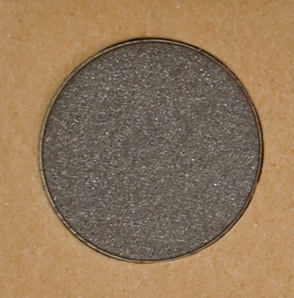 Fard à paupières gris rond dans un contenant marron. Le fard à paupières a une surface scintillante.
